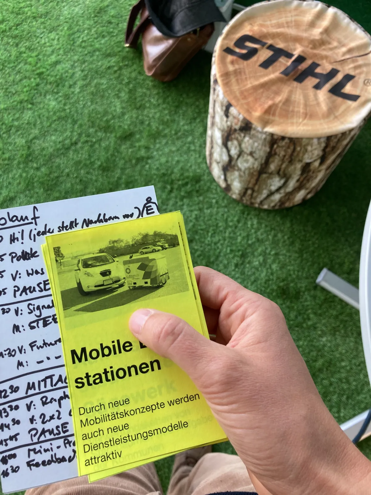 A workshop card on future mobile charging stations, held up next to a STIHL-branded seating prop at an outdoor workshop
